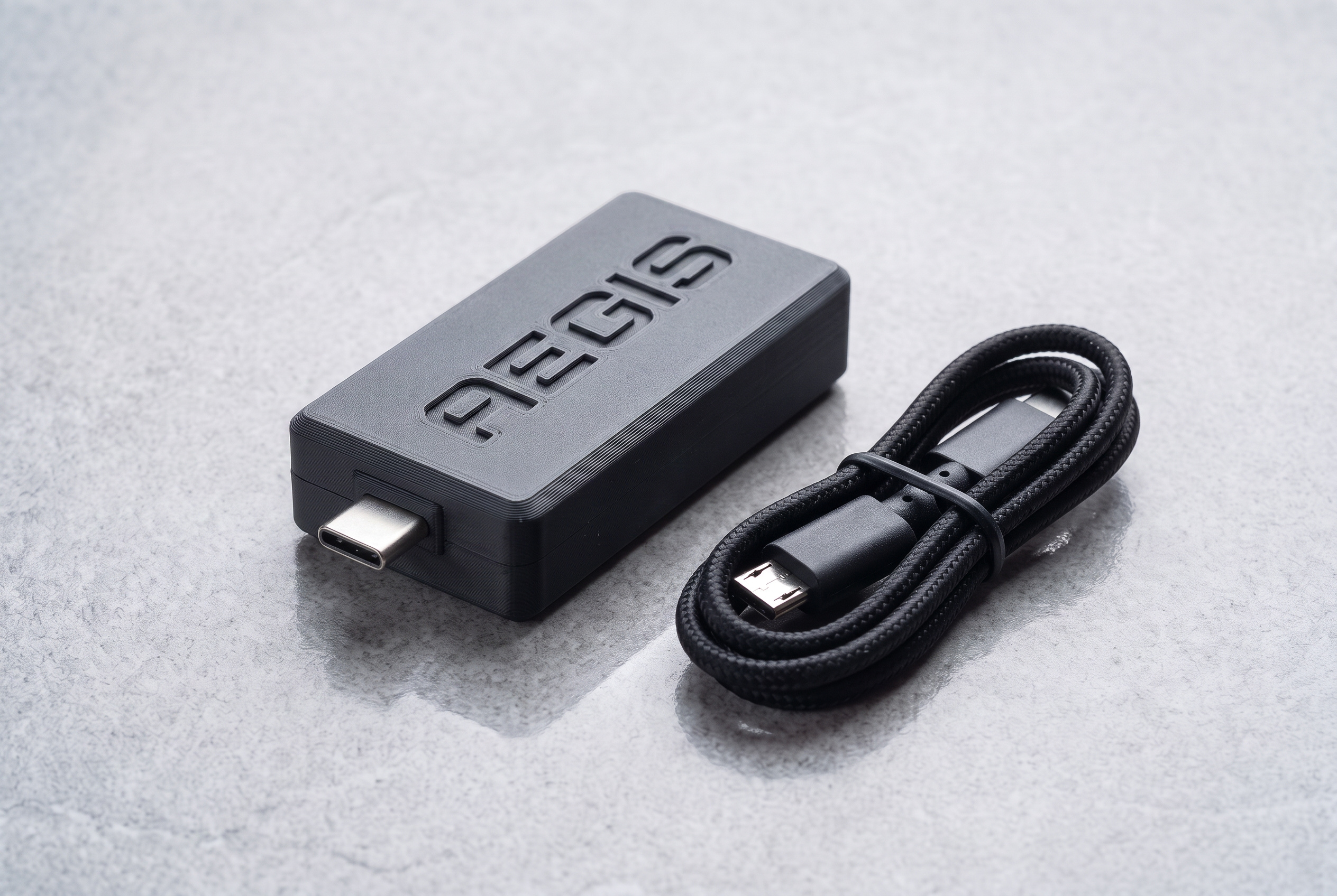 Matte black Aegis USB dongle with the name recessed on top, next to a coiled braided USB-C cable.